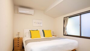 Quarto com cama, mesas de cabeceira, ar-condicionado, janela com cortinas e um quadro na parede.