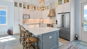 Une cuisine moderne avec des meubles blancs, un grand îlot central doté de tabourets, des appareils en acier inoxydable et un éclairage suspendu.