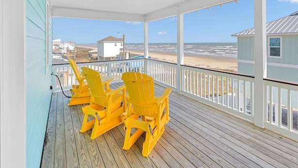 Une terrasse en bois avec une balustrade blanche, donnant sur une plage sous un ciel dégagé.