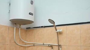 Un bagno con uno scaldabagno bianco montato a parete, collegato a una doccetta e a un rubinetto.