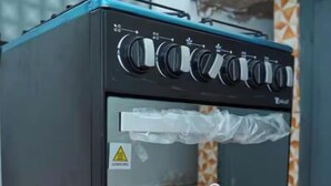 Un fornello a gas portatile con sportello in vetro, un’etichetta di avvertimento e un adesivo che indica una capacità di 4 fuochi.