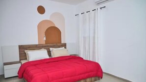 Una camera da letto con testiera in legno, copriletto rosso, cuscini bianchi e comodino.