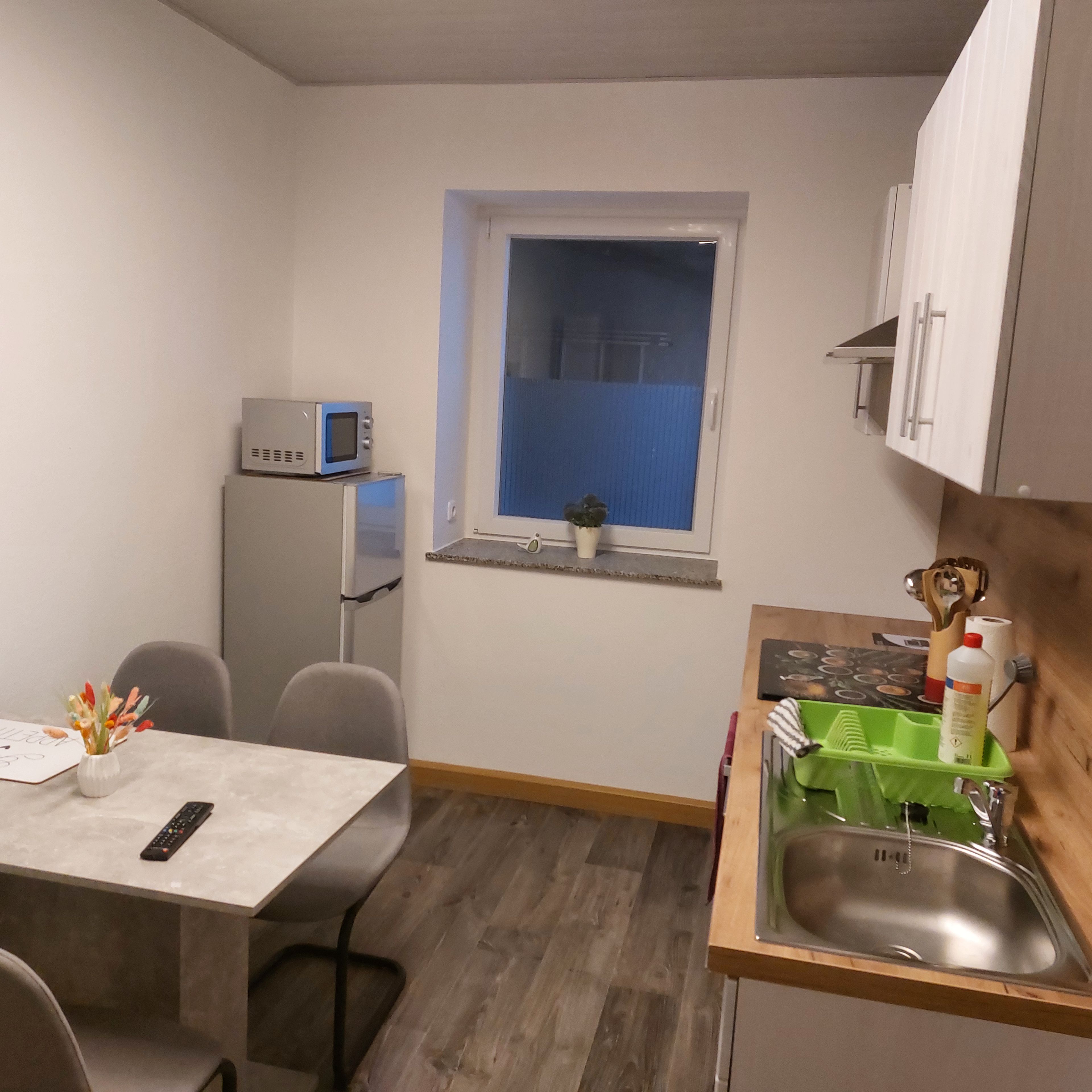 A compact kitchen with a refrigerator, microwave, sink, and a small window.