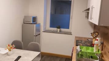 A compact kitchen with a refrigerator, microwave, sink, and a small window.