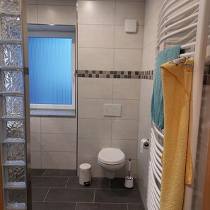 A bathroom with a toilet, a bidet, a trash bin, a towel rack with a towel, and a window with blinds. - "Am Schloss Hubertusburg" Vacation Rental, Centrally Located in Wermsdorf (Wermsdorf)