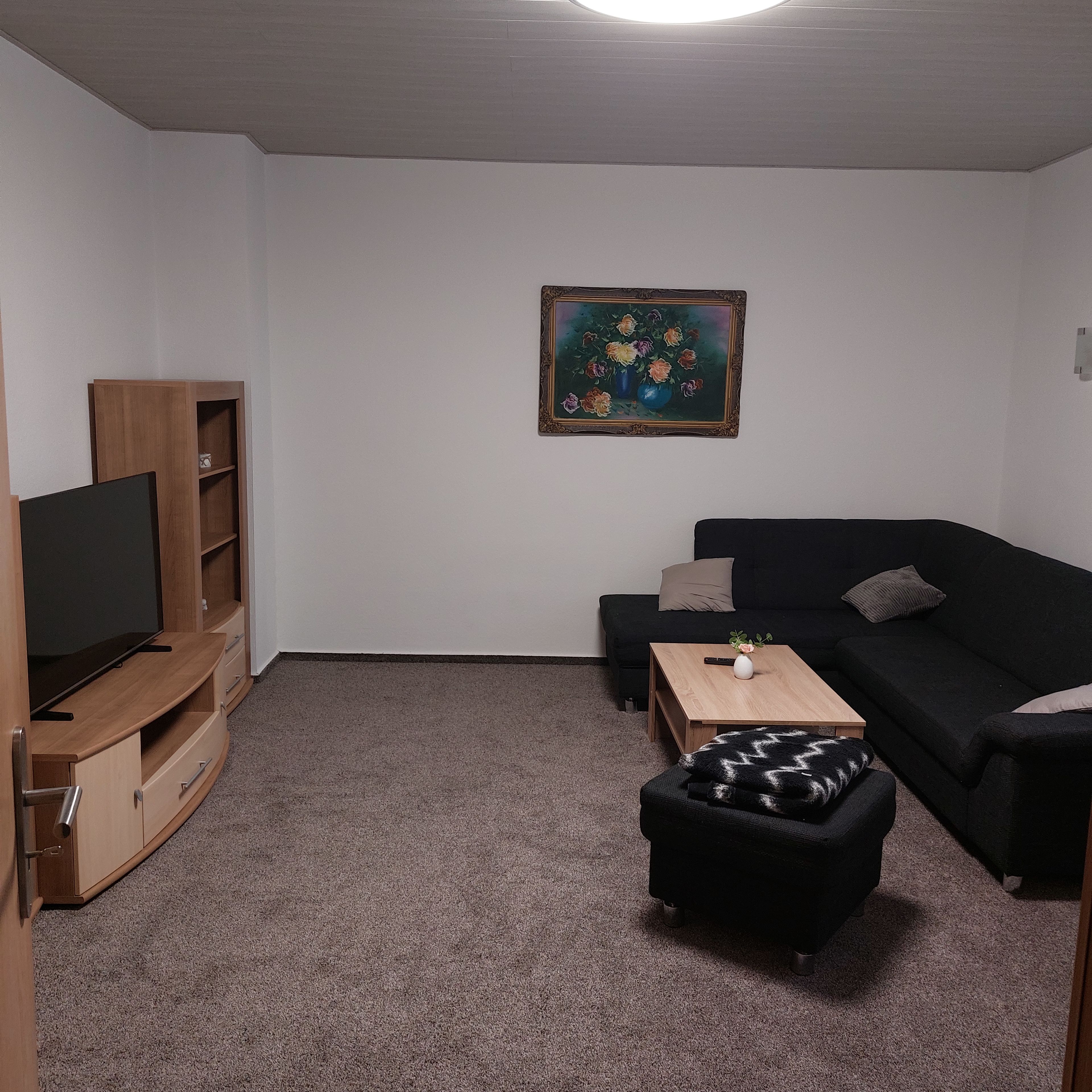 Una sala de estar con un televisor de pantalla plana, mueble de madera para equipo multimedia, sofá negro y una pequeña mesa de centro.