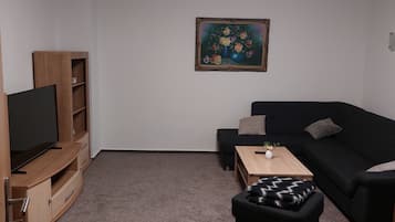 Una sala de estar con un televisor de pantalla plana, mueble de madera para equipo multimedia, sofá negro y una pequeña mesa de centro.