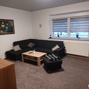 A living room with a black sofa, a wooden coffee table, and a black ottoman. There is a painting on the wall and a window with blinds. - "Am Schloss Hubertusburg" Vacation Rental, Centrally Located in Wermsdorf (Wermsdorf)