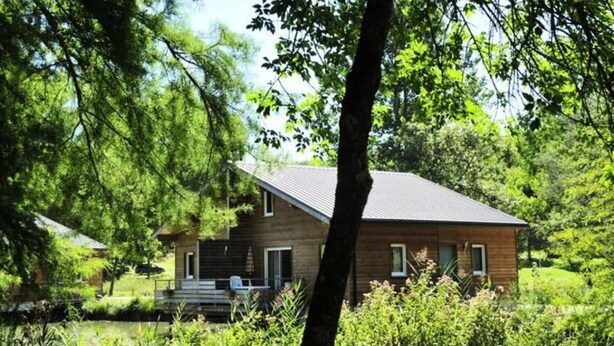 A wooden cabin with a sloped roof, surrounded by lush greenery and a small pond. - Cottage in Coly With Private Lake Access (La Cassagne)