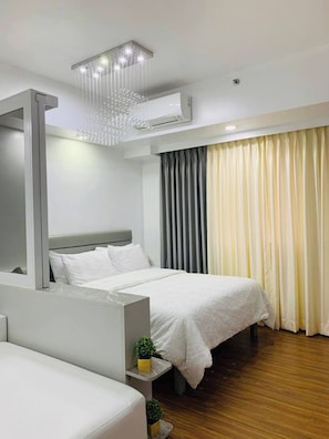 Une chambre d’hôtel moderne, équipée d’un lit, d’une table de chevet agrémentée d’une plante, d’un grand miroir et d’un appareil de climatisation fixé au plafond.