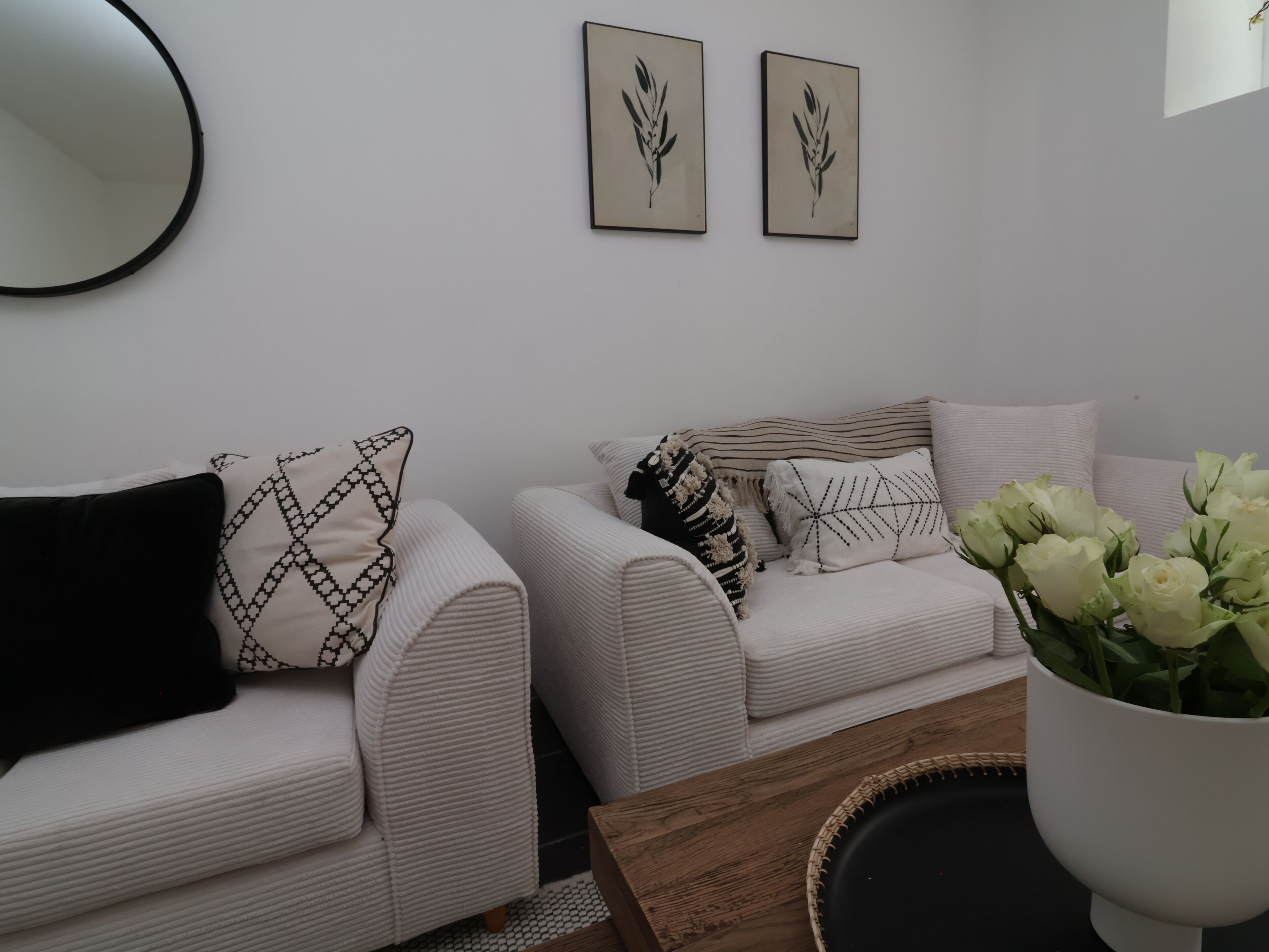 Una sala de estar con dos sofás blancos, un espejo redondo y dos cuadros enmarcados.