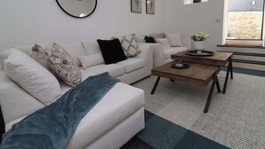 Un salon moderne avec un canapé, une table basse et des coussins décoratifs. On y trouve également des œuvres d’art murales et un miroir.