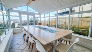 Une salle à manger baignée de lumière naturelle, avec une grande table et des chaises, de grandes fenêtres et une vue sur le jardin arrière.