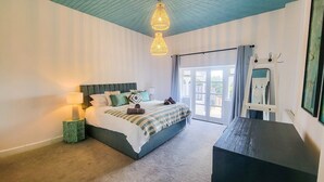 Une chambre à coucher avec un lit, des lampes de chevet, une commode et une grande fenêtre avec des rideaux.