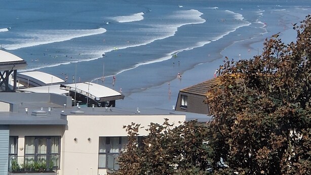 Une vue côtière avec une plage, des vagues et des bâtiments au premier plan.