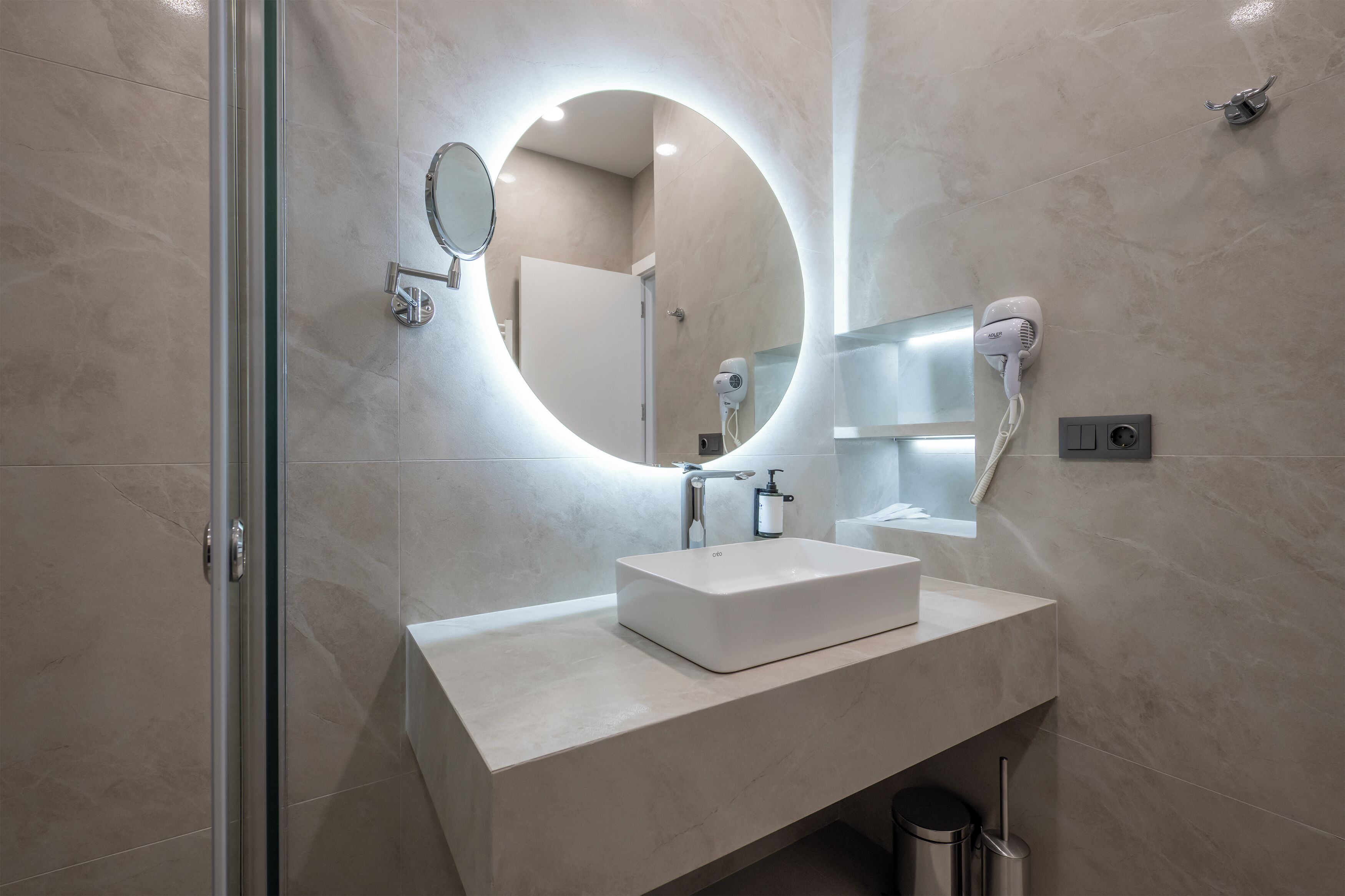 Un baño moderno con un espejo grande, una lámpara redonda y un secador de pelo.