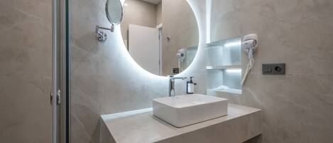 Un baño moderno con un espejo grande, una lámpara redonda y un secador de pelo.