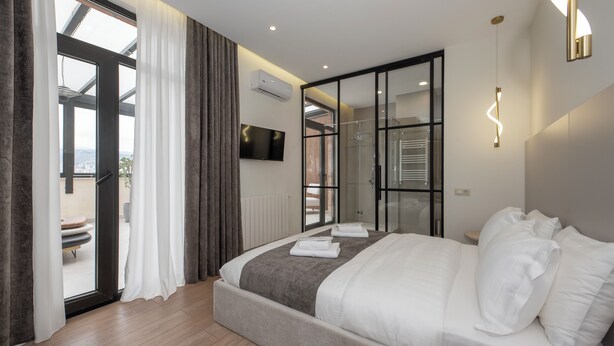 Une chambre moderne avec un grand lit, une télévision et une porte-fenêtre coulissante donnant sur un balcon.