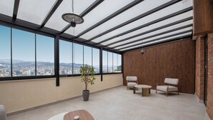 Une pièce moderne avec vue sur la ville, une table de massage en bois, deux chaises et une plante en pot.