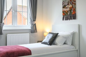 A neatly made bed with white and black pillows, a red throw blanket, and a window with curtains. - Host and Stay - The Rowton (Norwich)
