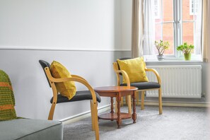 A room with two wooden chairs with yellow cushions, a small wooden table, and a window with a view of a brick building. - Host and Stay - The Rowton (Norwich)