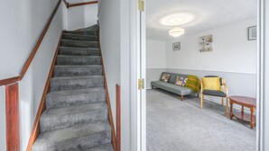 A staircase with carpeted steps and wooden handrails, leading to a living area with a sofa, chairs, and a small table. - Host and Stay - The Rowton (Norwich)
