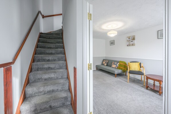 A staircase with carpeted steps and wooden handrails, leading to a living area with a sofa, chairs, and a small table. - Host and Stay - The Rowton (Norwich)