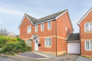 A two-story brick house with a white front door, a garage, and a small front yard with gravel and shrubs. - Host and Stay - The Rowton (Norwich)