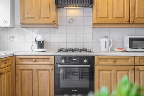 A kitchen with wooden cabinets, a Bosch oven, a coffee maker, and a microwave. - Host and Stay - The Rowton (Norwich)
