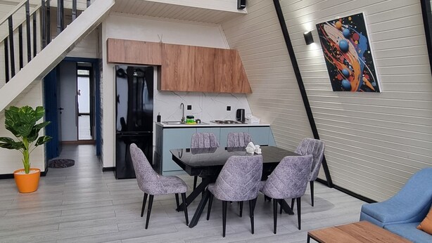 A spacious living area with a high ceiling, a staircase, a dining table with chairs, a sofa, and a kitchen area. - Cozy A-Frame house in Gabala.
Nature retreat with mountain view and Heated pool (Gebele)