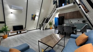 A modern living room with a sofa, coffee table, and TV. A staircase leads to a kitchen area with a dining table and chairs. - Cozy A-Frame house in Gabala.
Nature retreat with mountain view and Heated pool (Gebele)