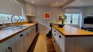 A modern kitchen with white cabinetry, a wooden countertop, and a central island. There is a window providing natural light and a view of the outdoors. - The Smarden Snug for Garden Lovers (Ashford)