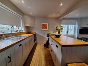 Una cocina moderna con armarios blancos, encimera de madera y una isla central. Hay una ventana que proporciona luz natural y vistas al exterior.