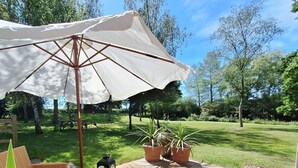 An outdoor patio with wicker furniture, a large umbrella, and potted plants. - The Smarden Snug for Garden Lovers (Ashford)