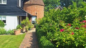 A brick pathway leading to a house with a distinctive conical roof structure. - The Smarden Snug for Garden Lovers (Ashford)