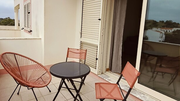 Ein Balkon mit Tisch und vier Stühlen, eine Schiebetür aus Glas und Blick auf die Landschaft.