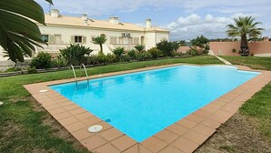 Ein rechteckiger Swimmingpool mit Fliesenbordur, umgeben von einer Rasenfläche und Palmen.