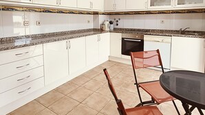 Eine moderne Küche mit weißen Schränken, einer Granit Arbeitsplatte, einem Geschirrspüler und einem Essbereich mit einem Glastisch und Metallstühlen.