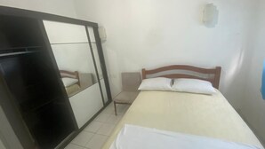 A bedroom with a bed, a wooden headboard, a bedside table, a chair, a wardrobe, and a mirror. - Hostel Suites (Recife)