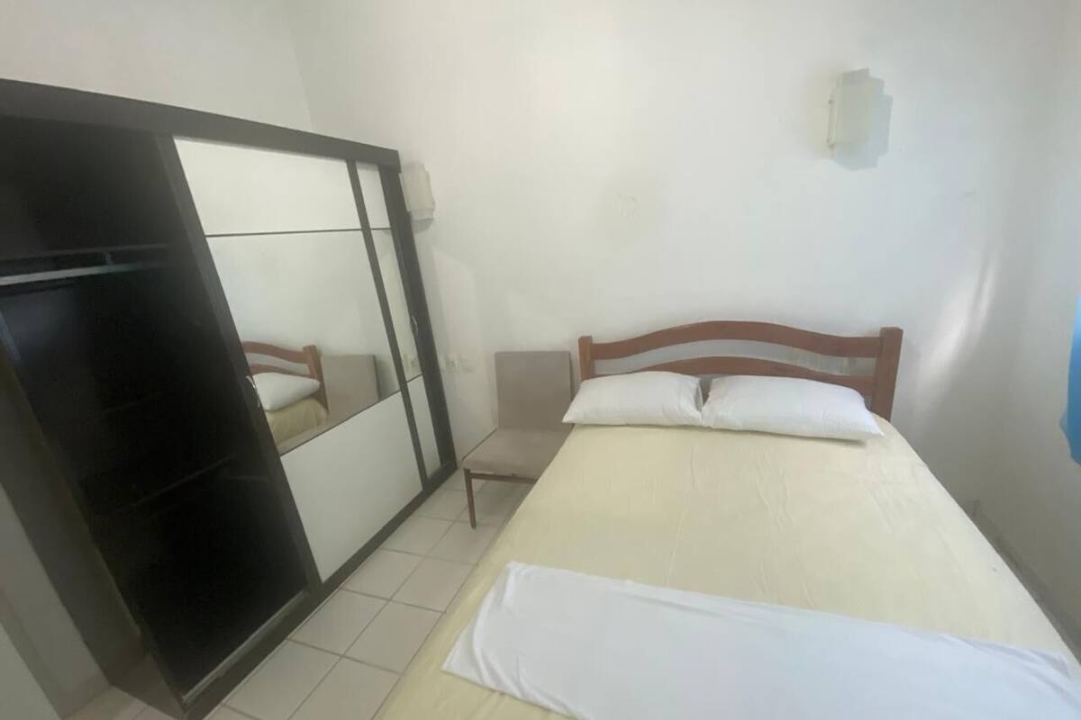 Un dormitorio con una cama, cabecera de madera, mesita de noche, una silla, armario y un espejo.
