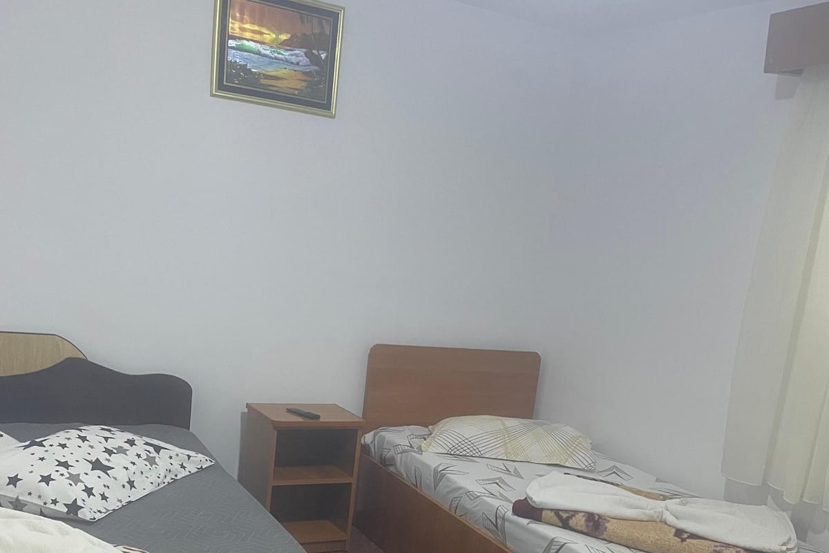 A hotel room with two single beds, a wooden headboard, a small bedside table, and a wall-mounted picture.