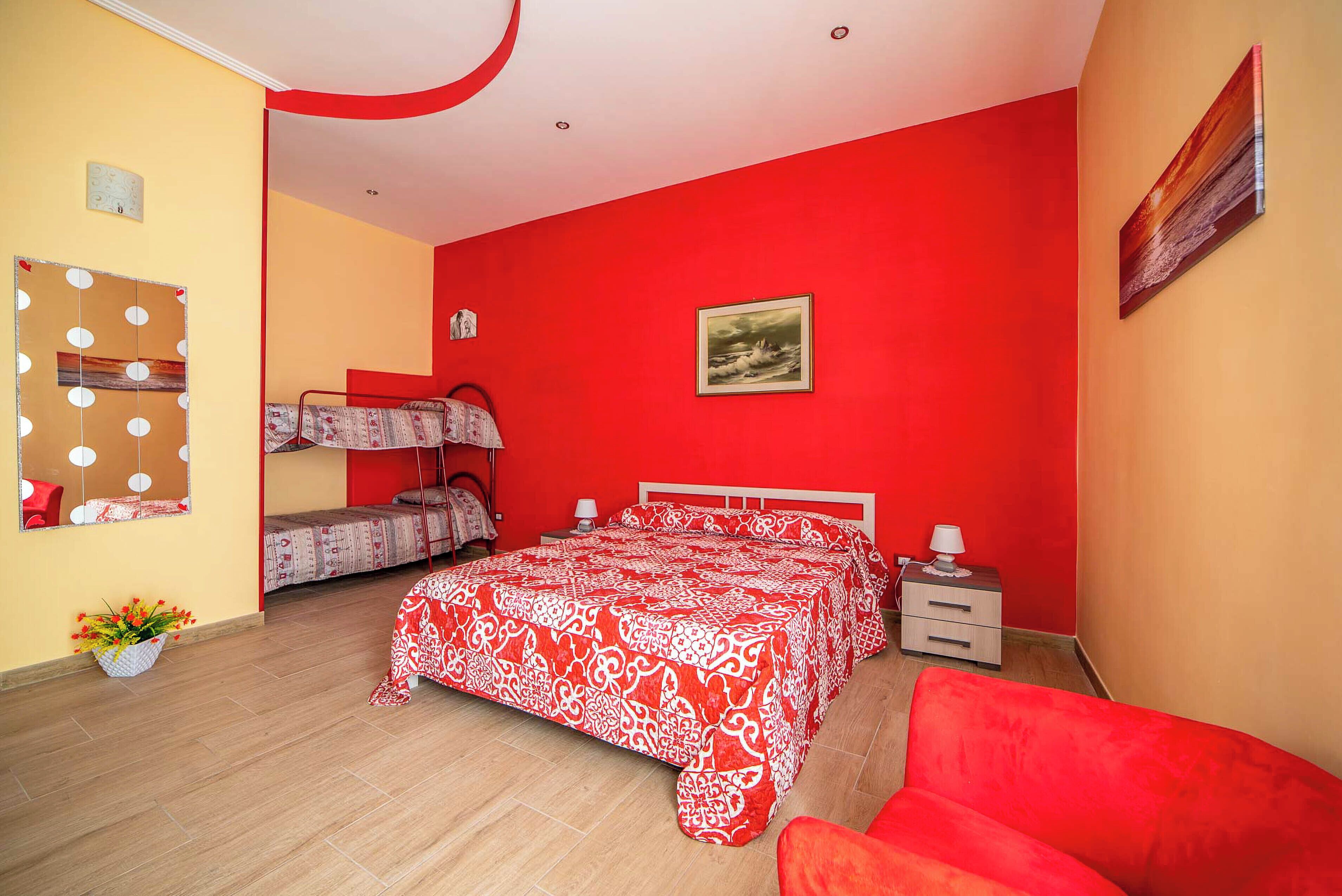 A bedroom with a red and white bedspread, a bunk bed, a nightstand, and a red chair.