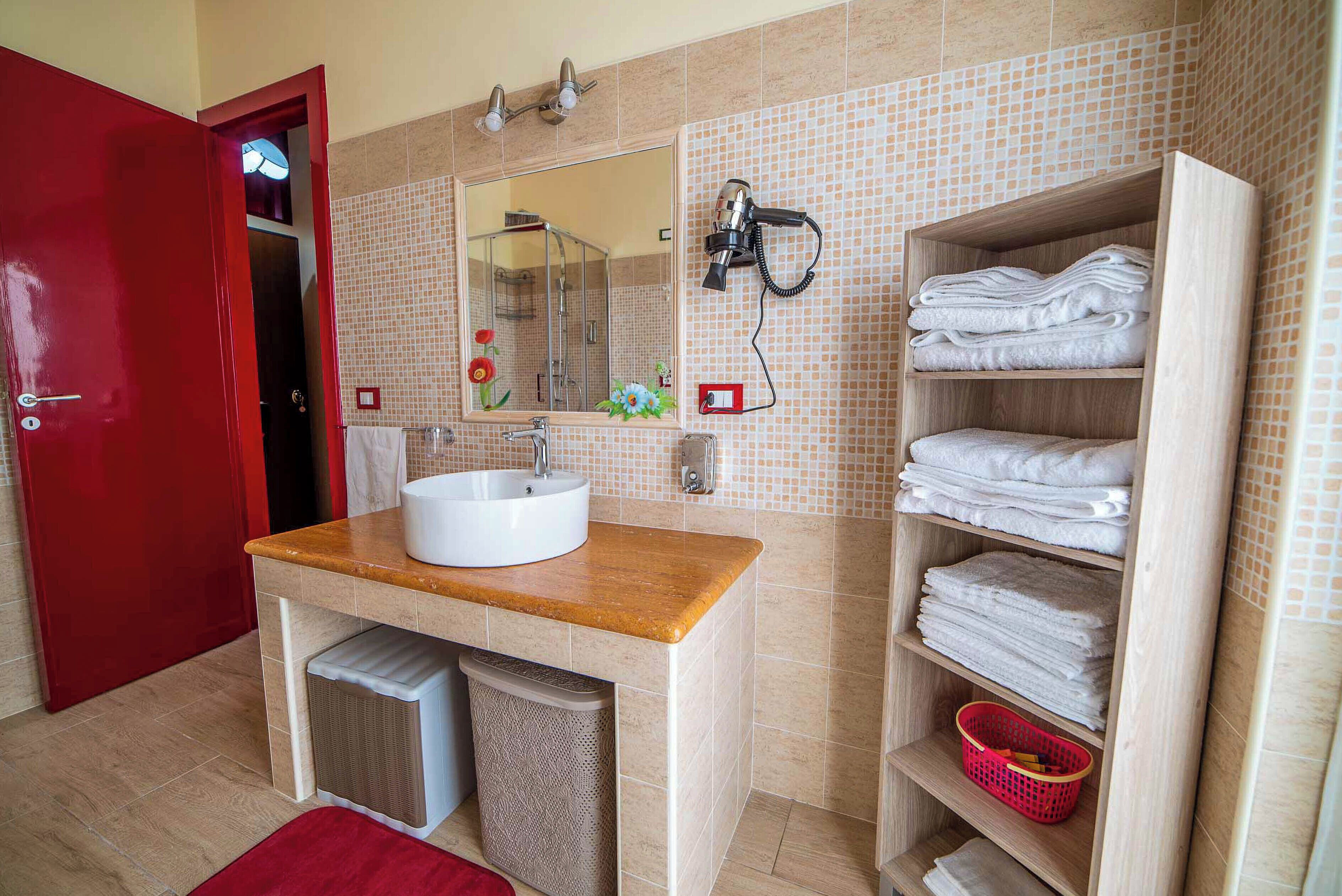 A bathroom with a sink, mirror, towel rack, and a red door.