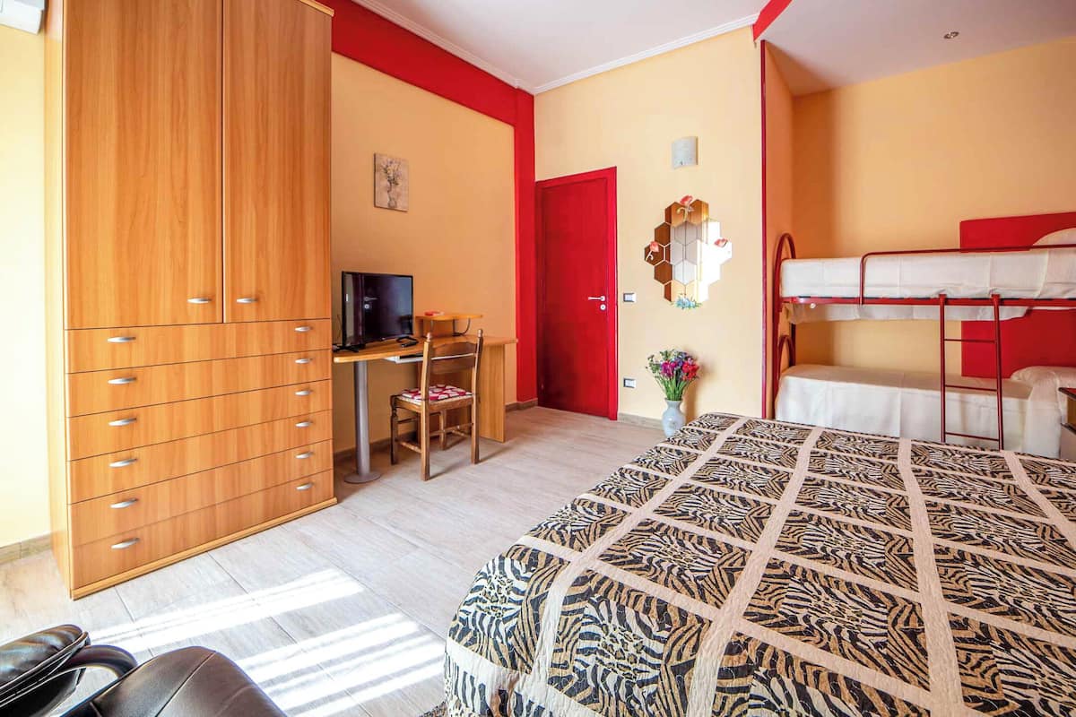 A room with a bed, a wardrobe, a desk, a chair, and a television.