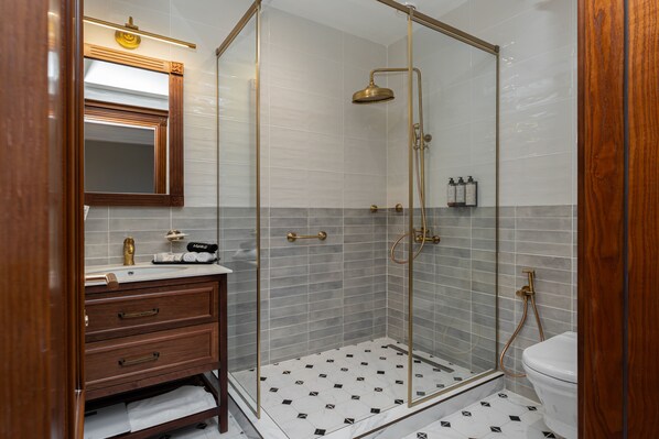 Une salle de bain dotée d’une douche à parois de verre, d’un meuble-lavabo en bois avec des tiroirs, de toilettes et d’un miroir avec un cadre doré.