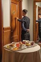 Een hotelkamer met een houten deur, een ronde tafel met een dienblad eten en een spiegel die de kamer weerspiegelt.