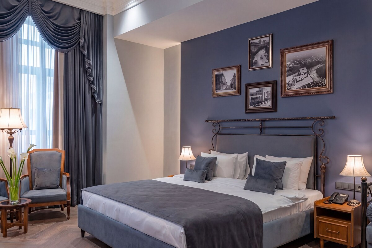 Habitació d'hotel amb un llit gran, dues taules de nit, una cadira i una paret amb quadres.