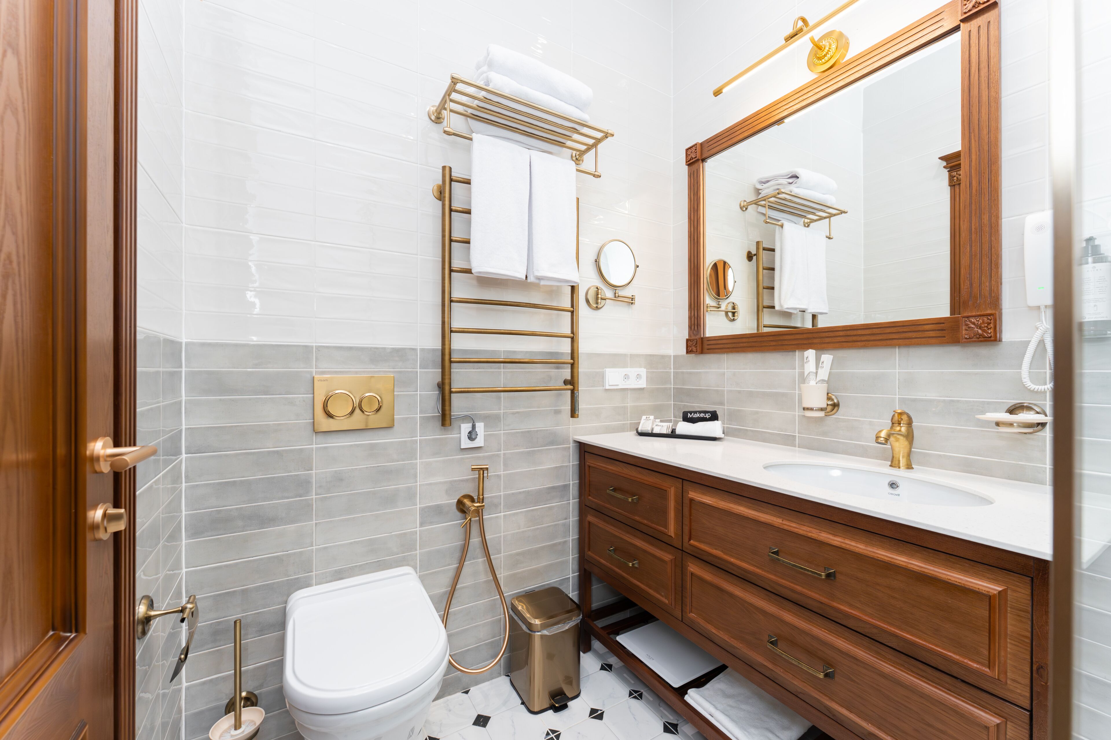 A modern bathroom with a white toilet, a gold vanity, a large mirror, and a towel rack.