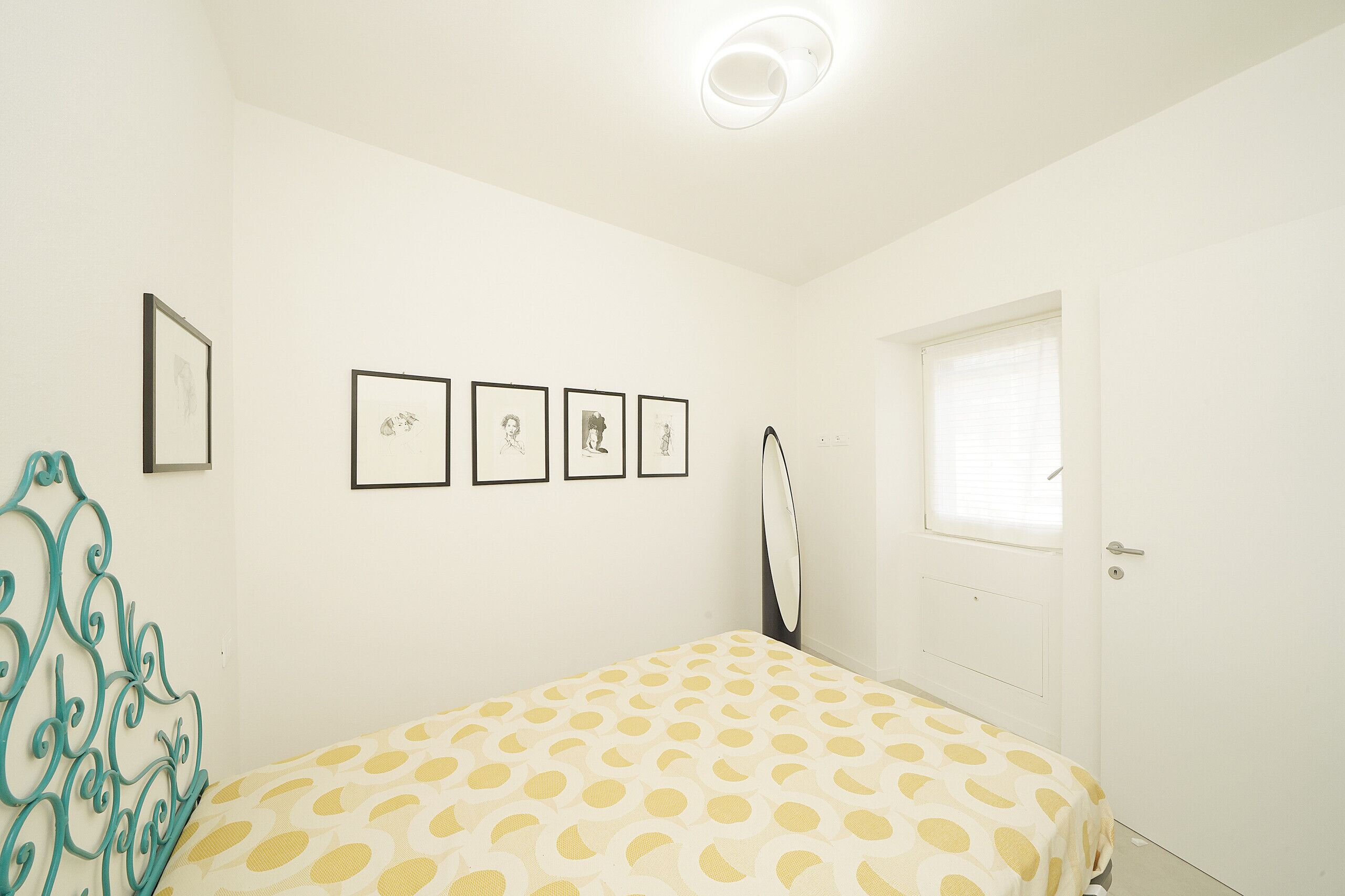 A bedroom with a bed, a door, a window, and four framed pictures on the wall.