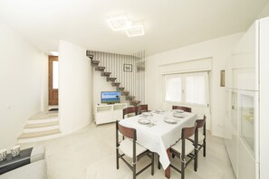 A dining area with a table set for six, a staircase, and a television on a stand. - Casa all Angolo Relax (Toscolano Maderno)